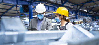 在冠状病毒大流行期间，工人戴着防护口罩。带口罩的工业主管经理控制生产工厂的工人。