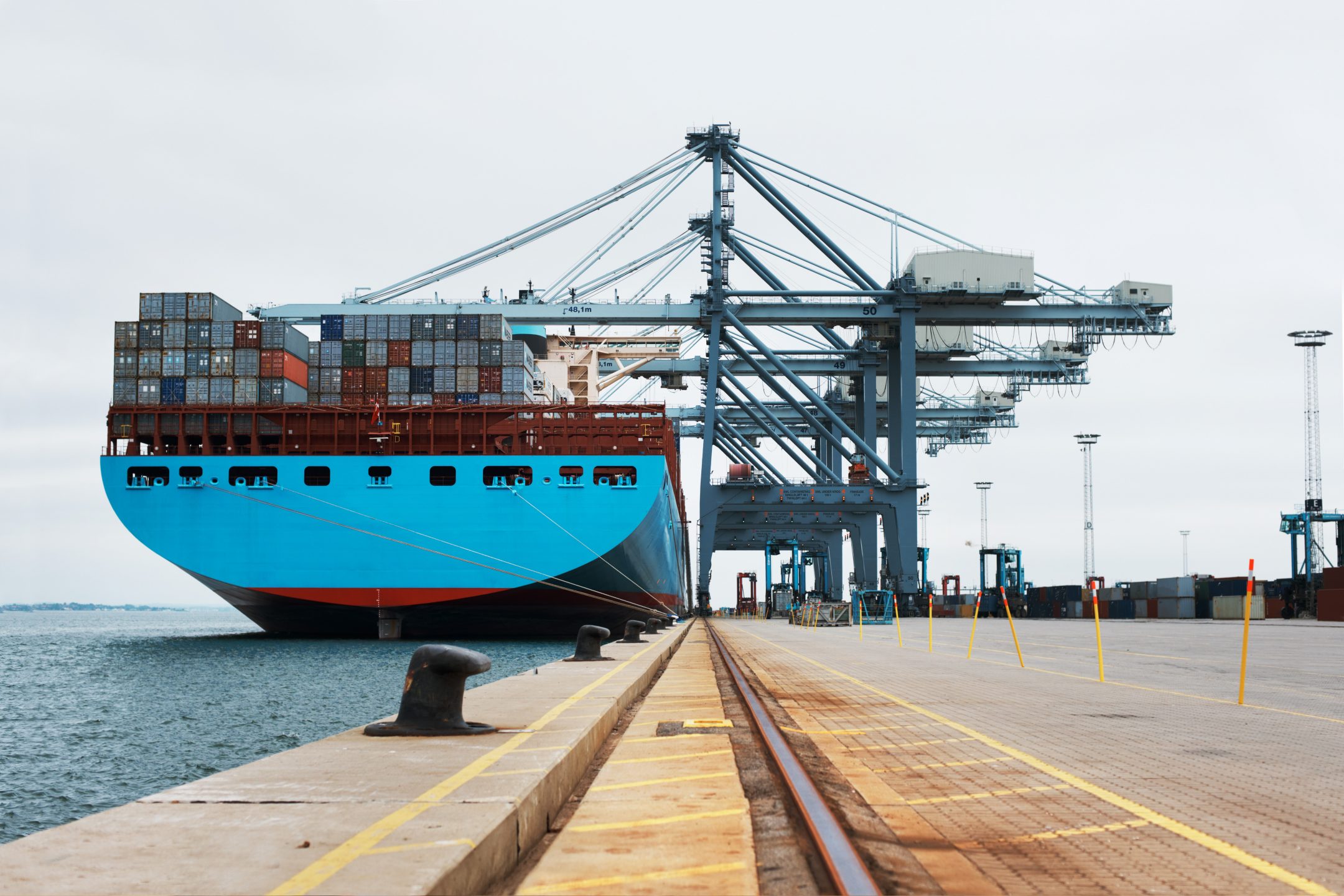 一艘满载货物的集装箱船停靠在港口边上，用起重机为其提供服务。