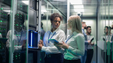 中景:两名妇女在数据中心和成排的服务器机架一起工作，检查设备，讨论工作